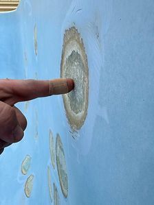 Finger touching an oval target on a blue wall surface, likely a bullet or impact mark