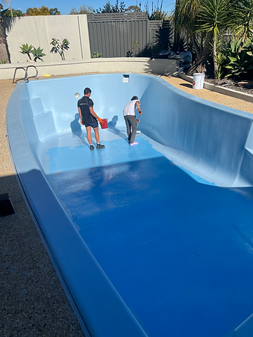 Two people standing in an empty blue swimming pool on a sunny day