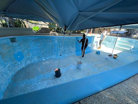 Underwater pool repair workers cleaning a drained blue pool under a canopy