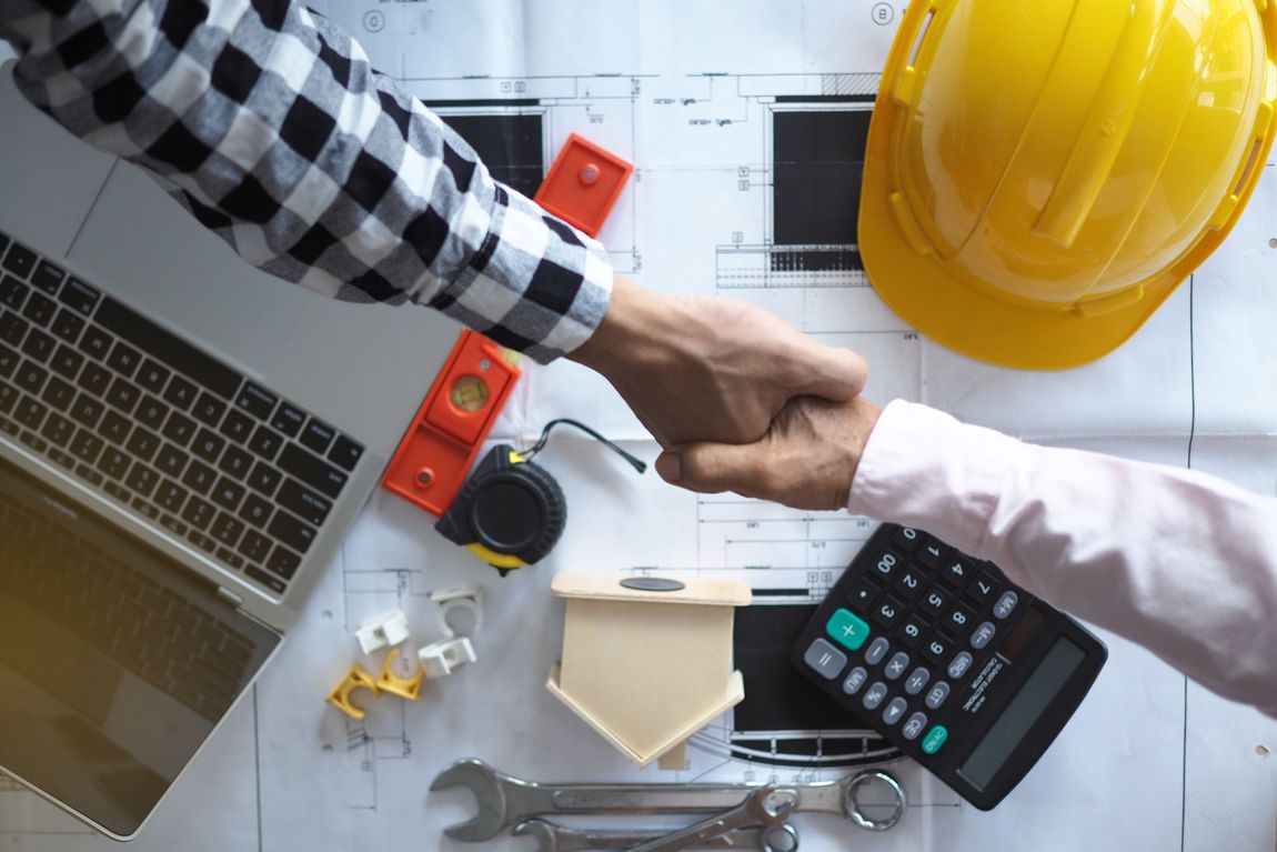 Two construction workers are shaking hands over a blueprint.