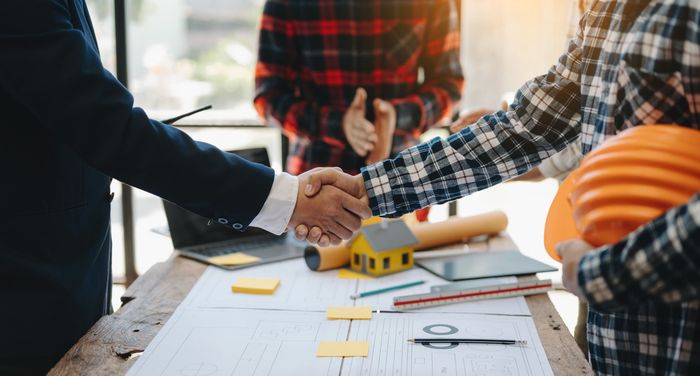 A group of construction workers are shaking hands over a table.
