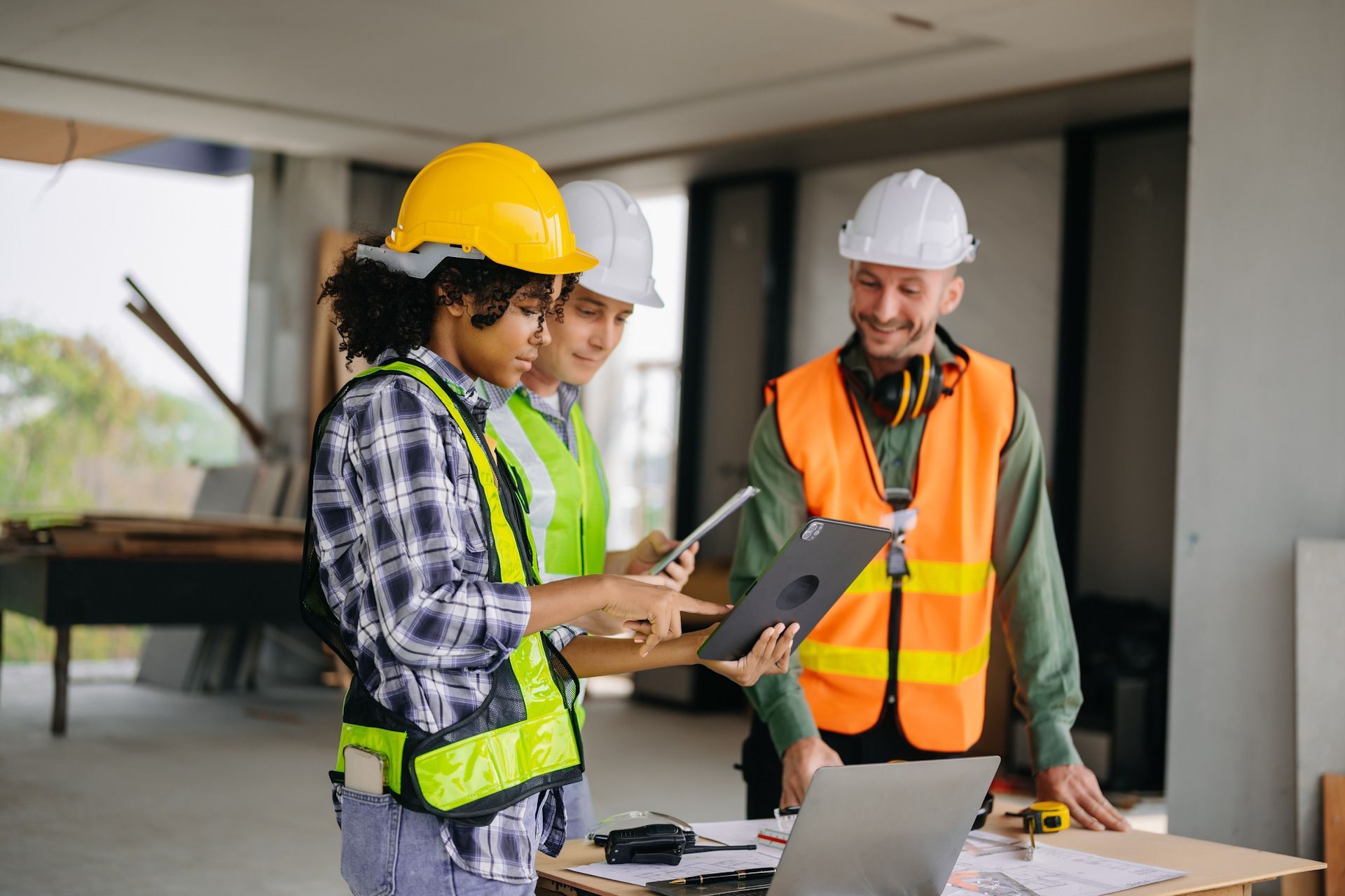 A group of construction workers are standing around a table looking at a tablet.