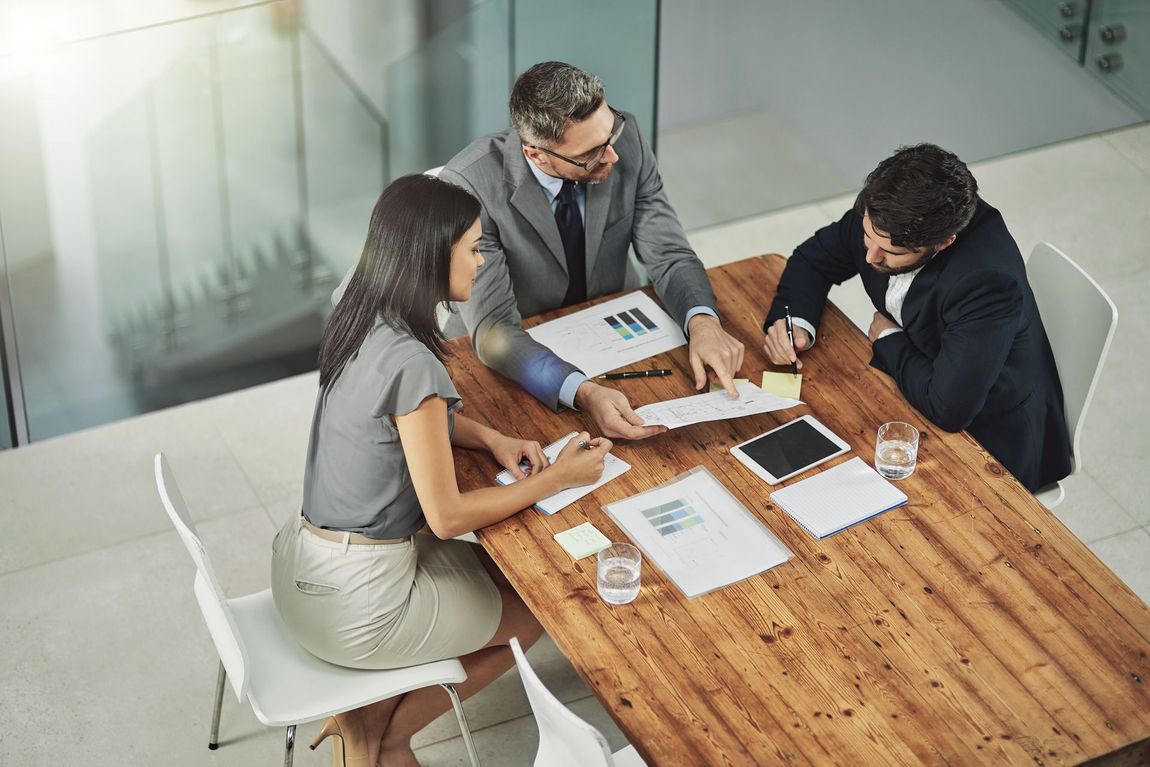 A group of business people are sitting around a wooden table having a meeting.