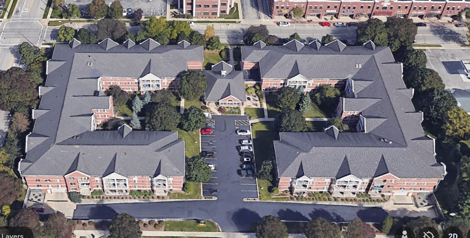Aerial view of a U-shaped red brick apartment complex with grey shingled roofs and a central parking lot.