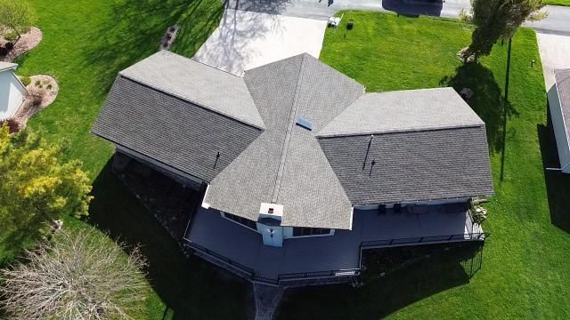 An aerial view of a gray-roofed house with a large deck and a spacious backyard in a suburban setting.