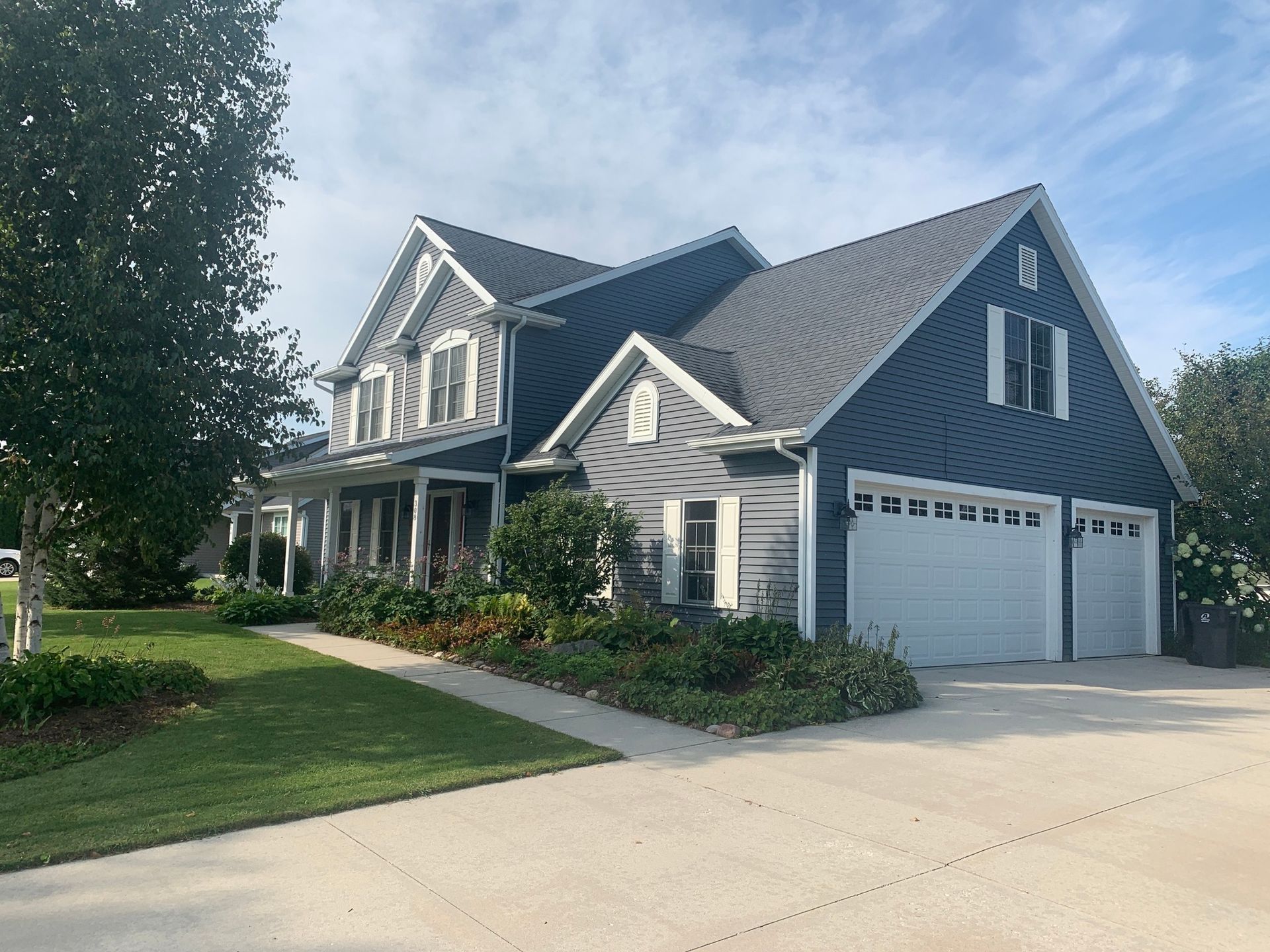 A blue two-story house with a white-trimmed garage and porch, situated on a lawn with a concrete driveway.