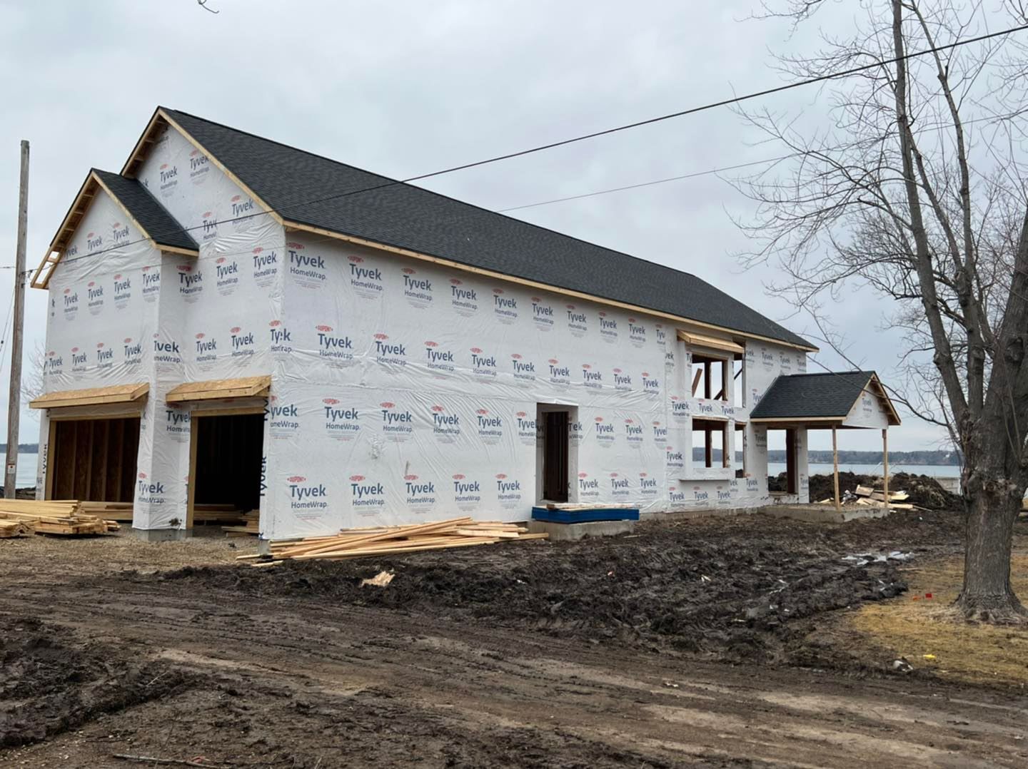 A new two-story house under construction, wrapped in white protective sheeting, with an attached garage and a lake view.