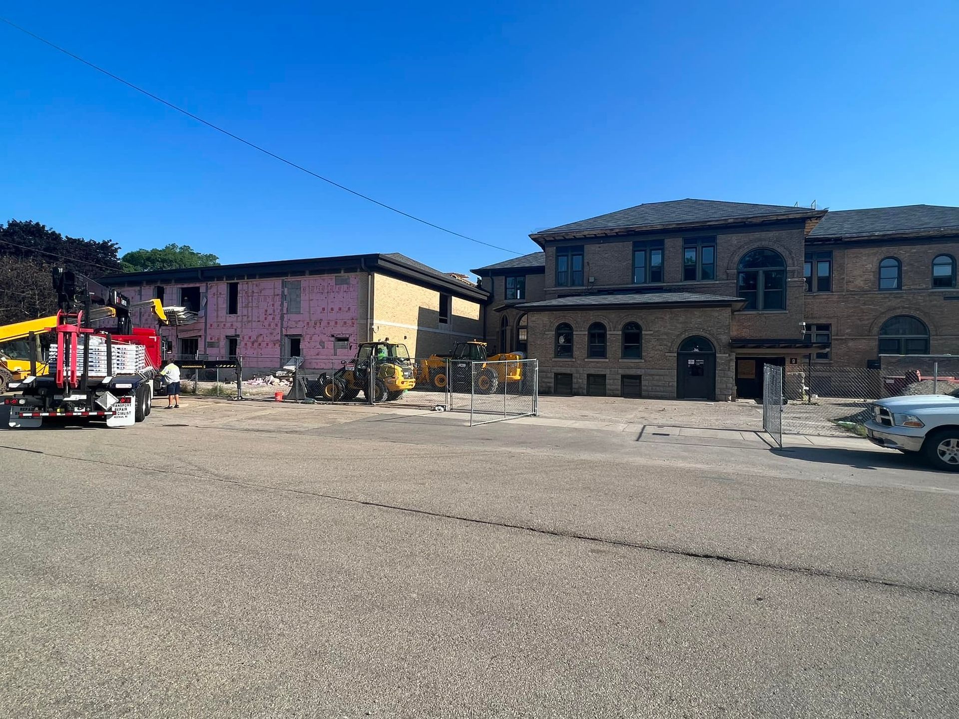 Construction site with a red truck, heavy equipment, and a brick building undergoing renovation under a clear blue sky.