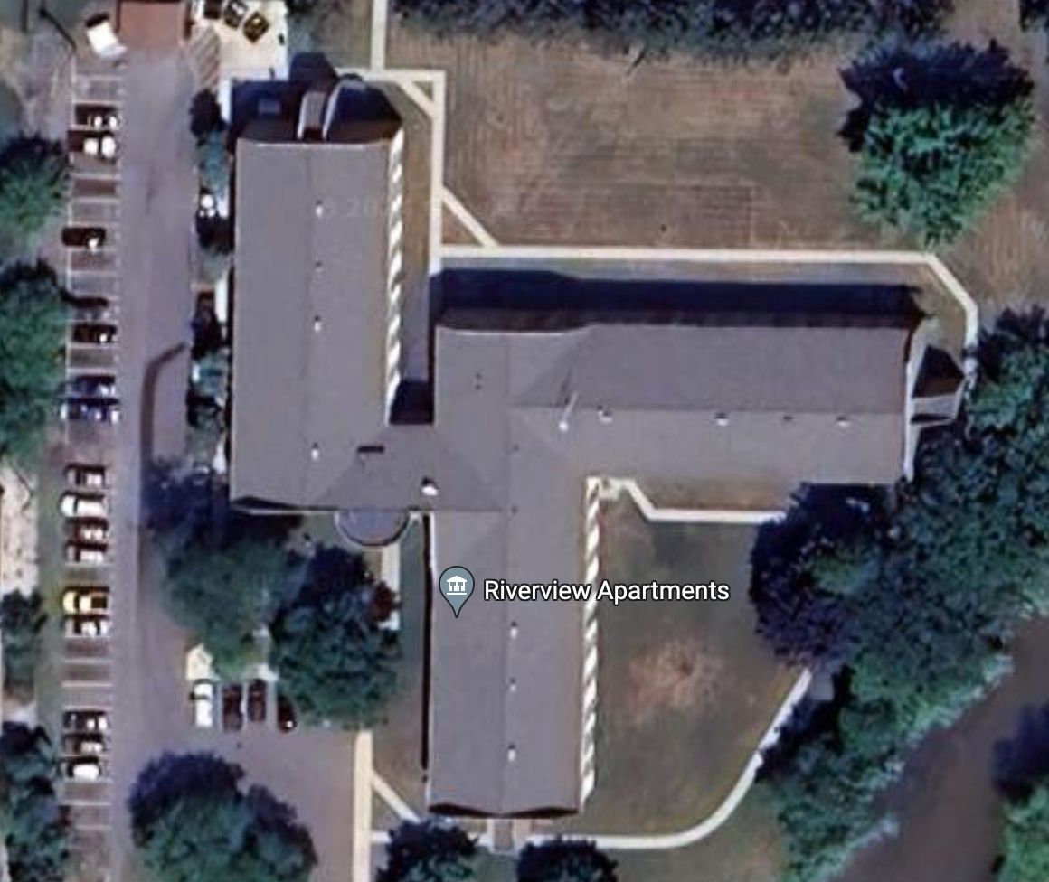 Aerial view of Riverview Apartments, a multi-wing building surrounded by parking lots and trees.