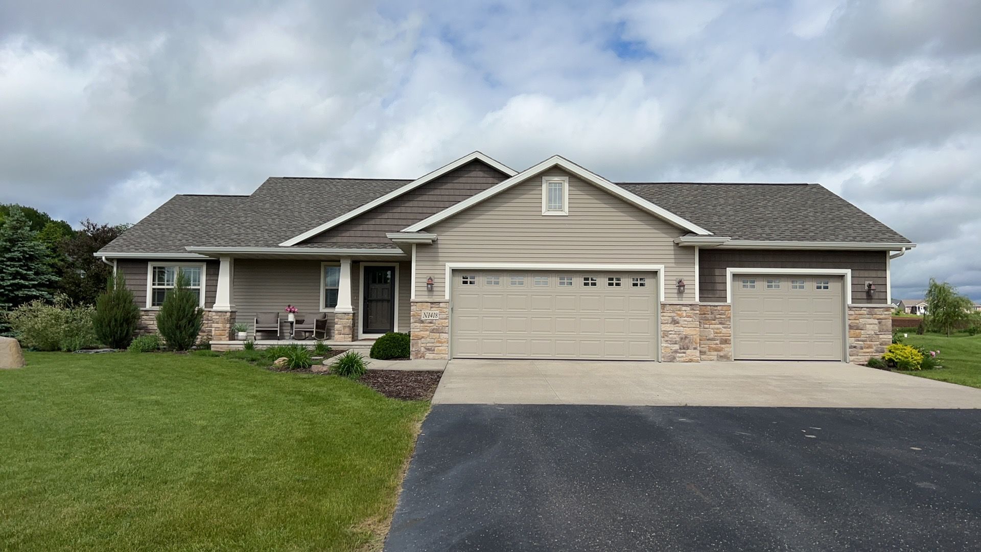 A single-story suburban house with beige siding, stone accents, a gray shingled roof, and a three-car garage.