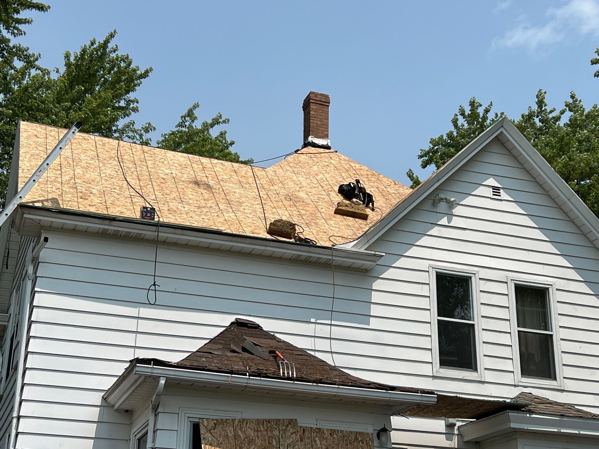 A house under renovation with new plywood roof decking and a brick chimney against a blue sky.