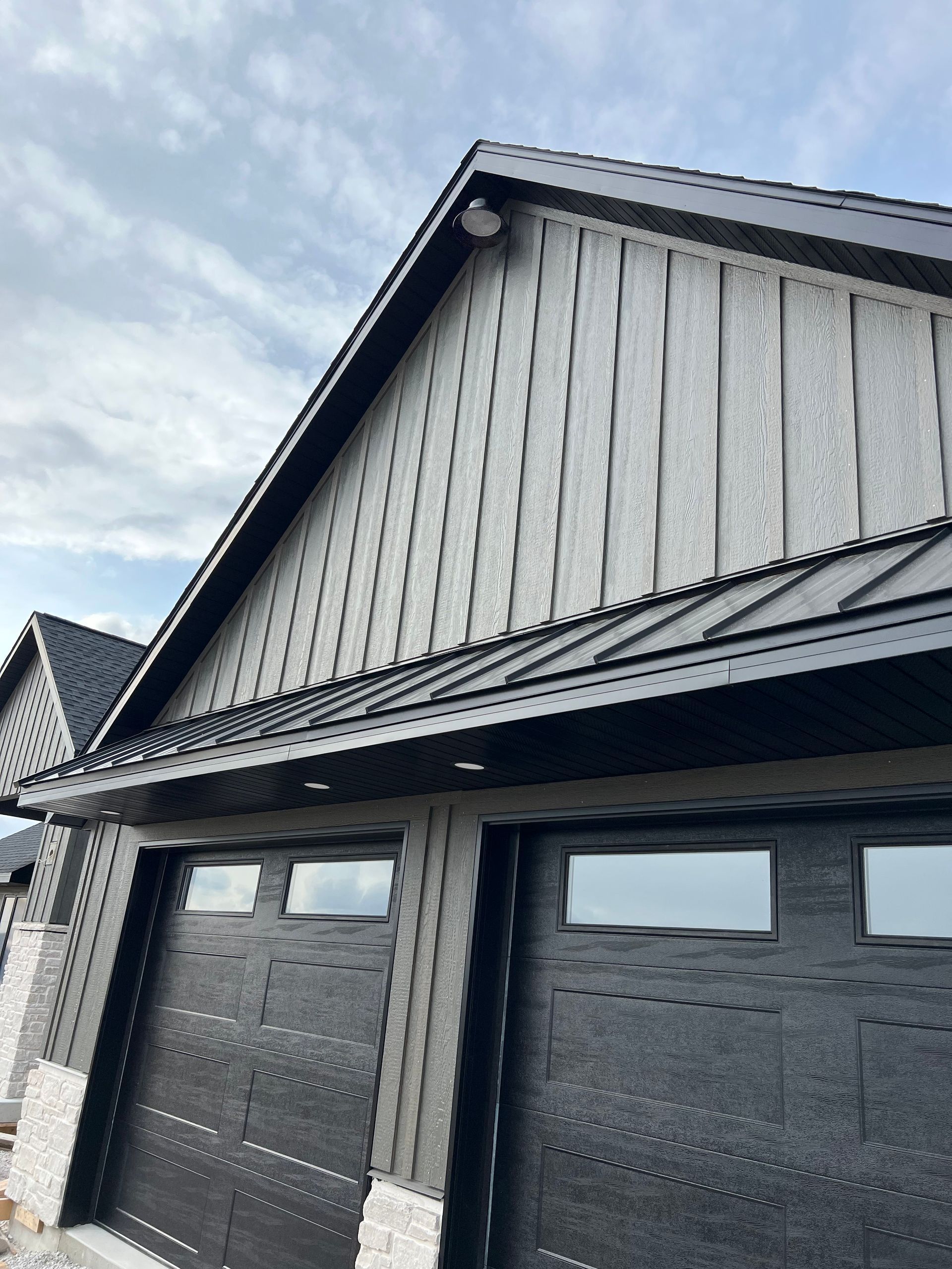 A low-angle view of a garage gable with vertical grey siding, a black metal roof, and two dark garage doors.