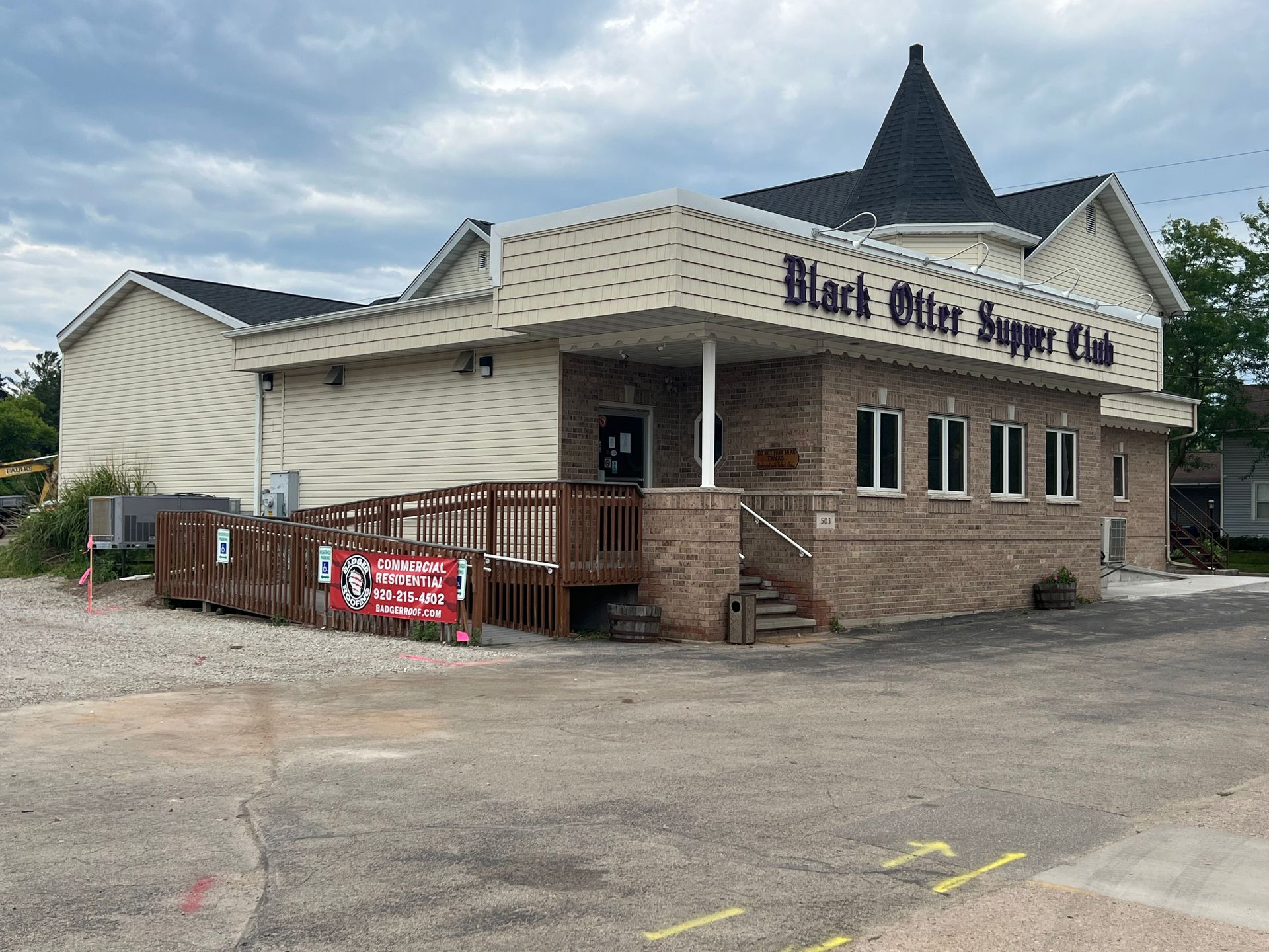 The Black Otter Supper Club, a brick building with a pointed roof and a wooden wheelchair ramp, under a cloudy sky.