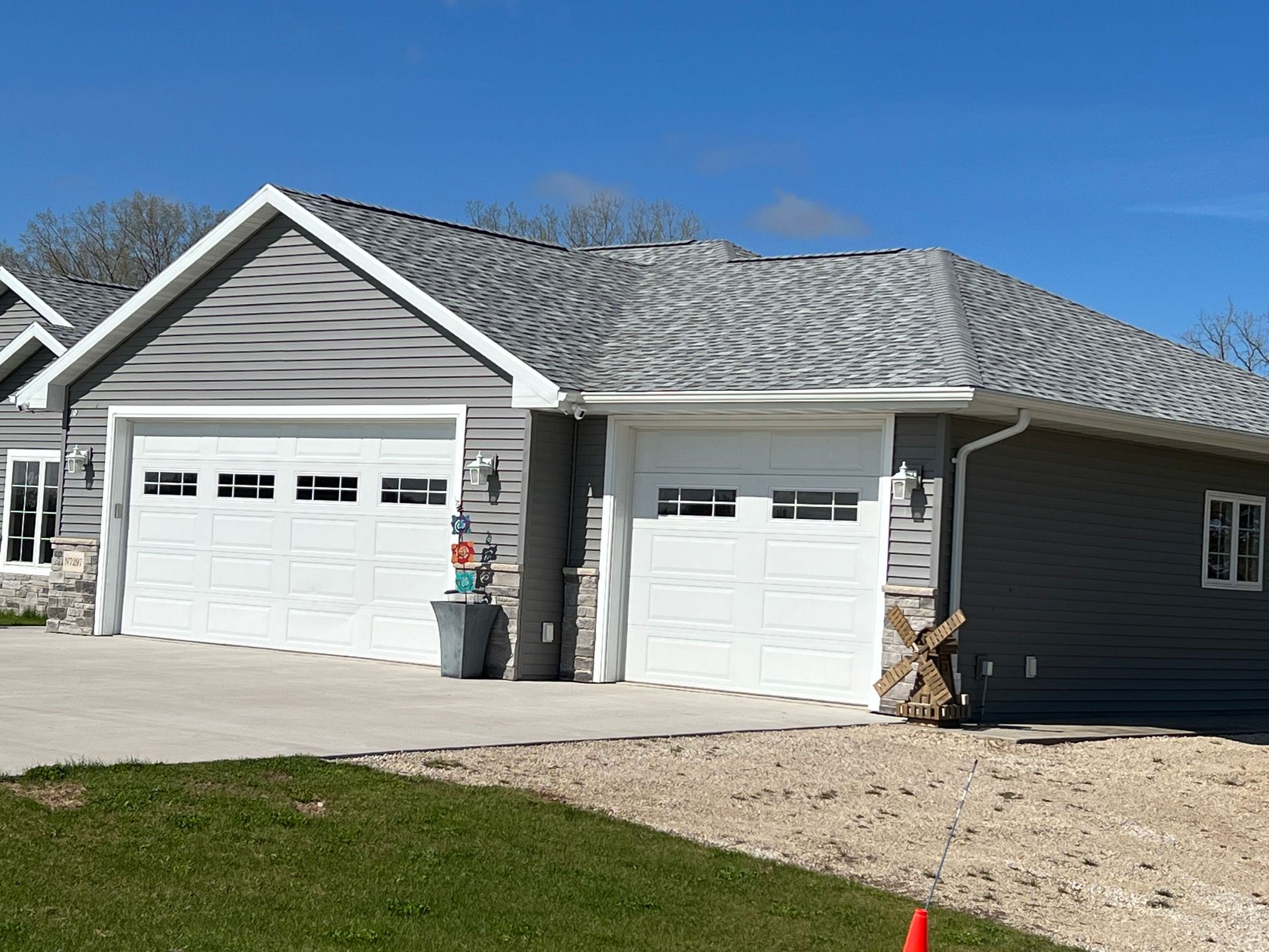 A grey, single-story house with a three-car garage, white trim, and a stone facade, set against a bright blue sky.