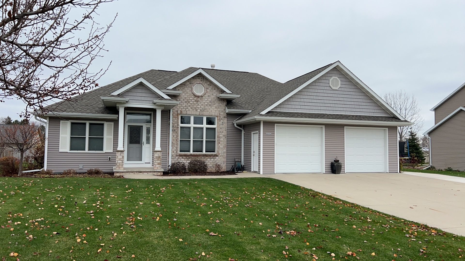 A one-story suburban home with light gray siding, a brick facade, a two-car garage, and a front lawn under a cloudy sky.