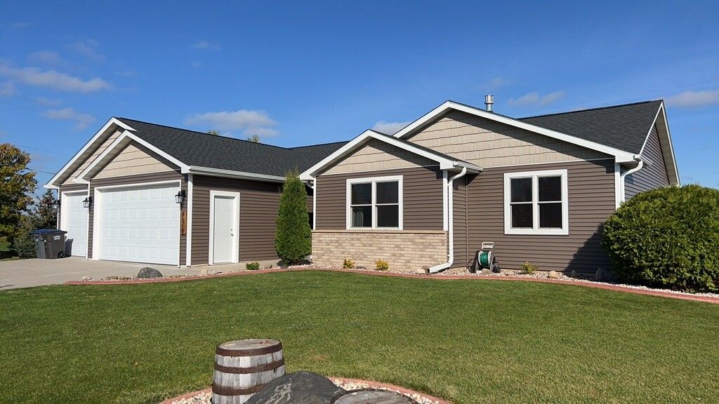 A single-story suburban house with brown horizontal siding, tan stone accents, white trim, and a dark shingled roof.