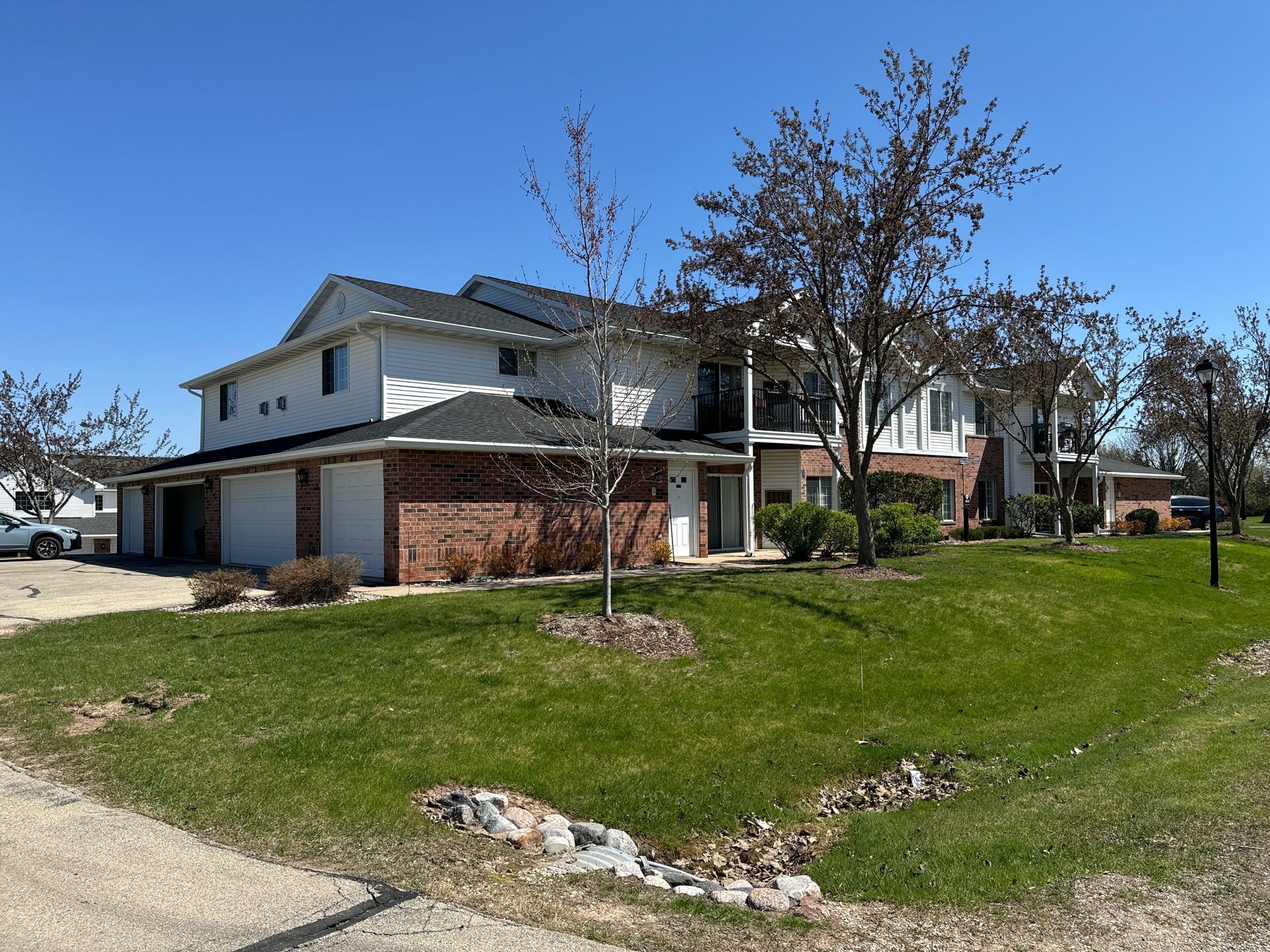 A two-story apartment complex with white siding and brick accents, surrounded by a green lawn and leafless trees.