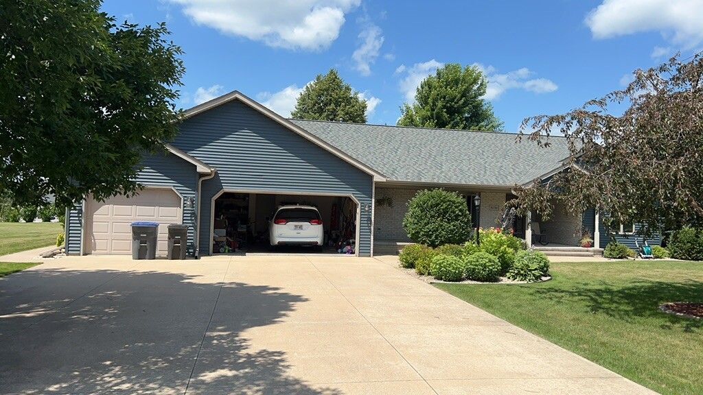 Single-story house with blue siding, a two-car garage, and a large concrete driveway under a sunny sky.