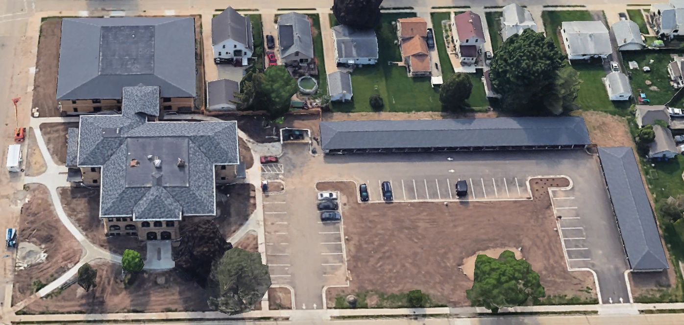 Aerial view of a complex with a large multi-story building, an adjacent parking lot, and two long, one-story buildings.