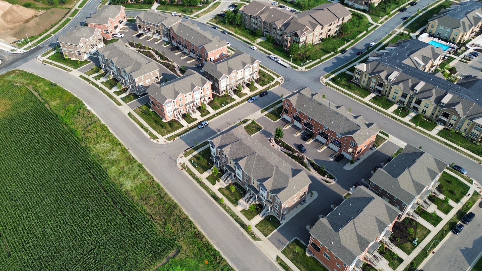 Aerial view of a suburban neighborhood with rows of houses, streets, and adjacent green fields