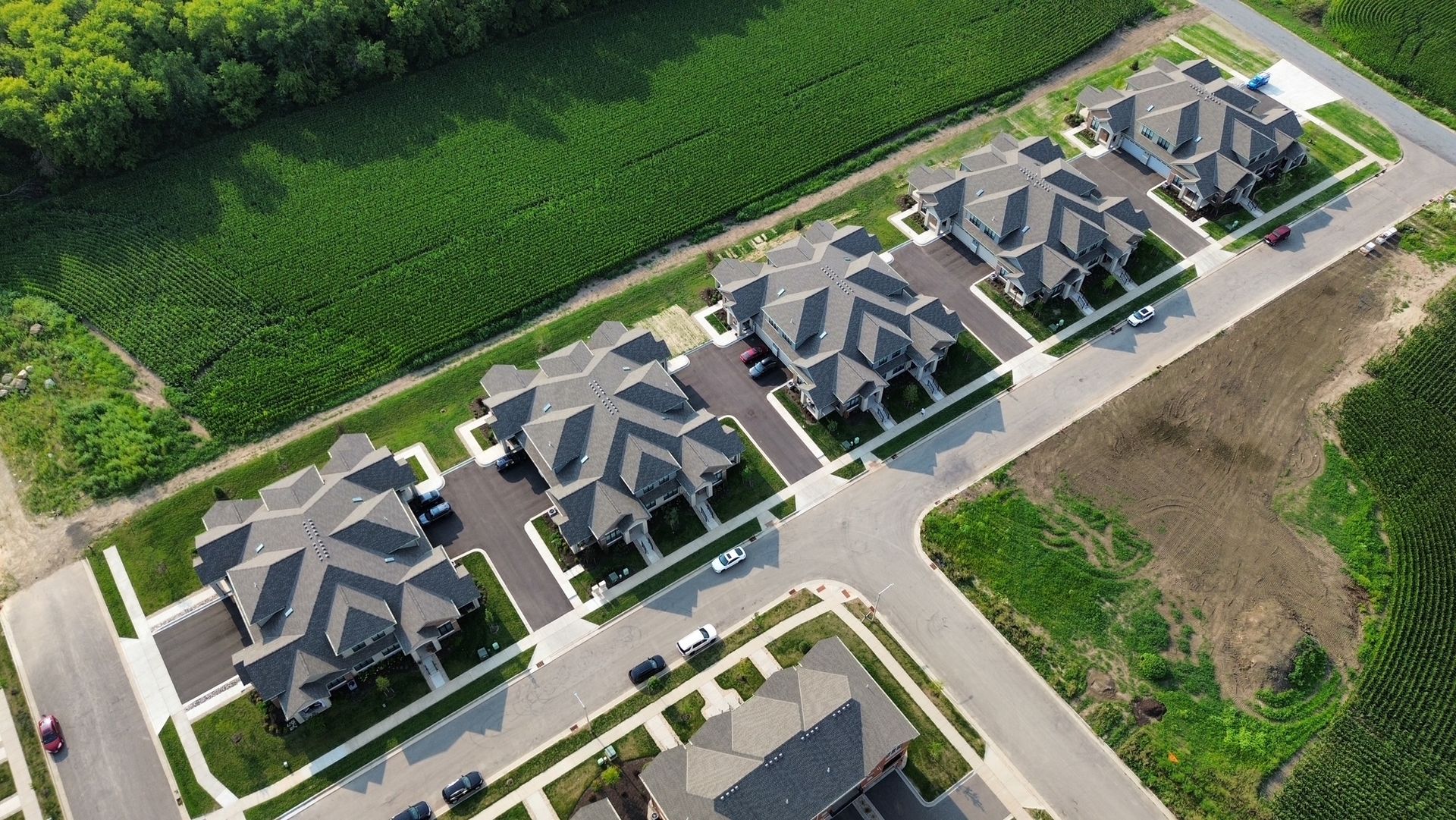 Aerial view of a row of modern suburban houses beside green fields and roads.