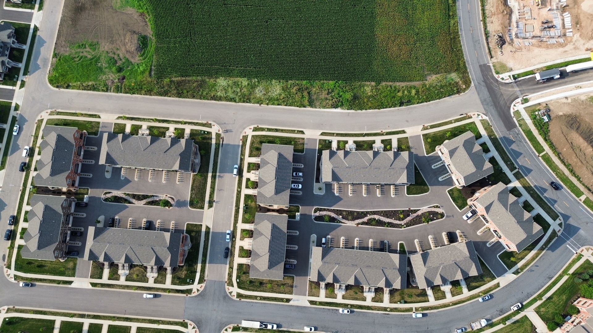 Aerial view of a suburban apartment complex with parking lots, roads, and green grass fields nearby