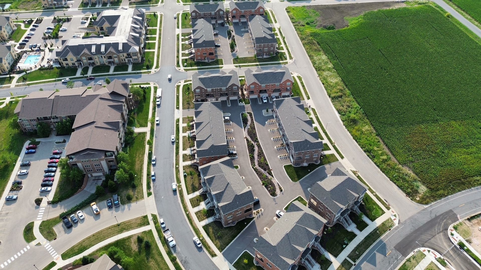 Aerial view of a suburban neighborhood with rows of houses, streets, and a large green field.