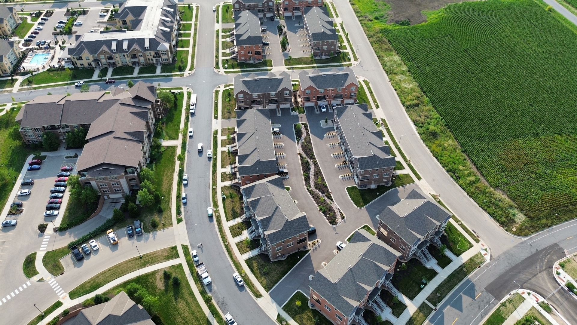 Aerial view of a suburban apartment complex beside a curving road and green field.