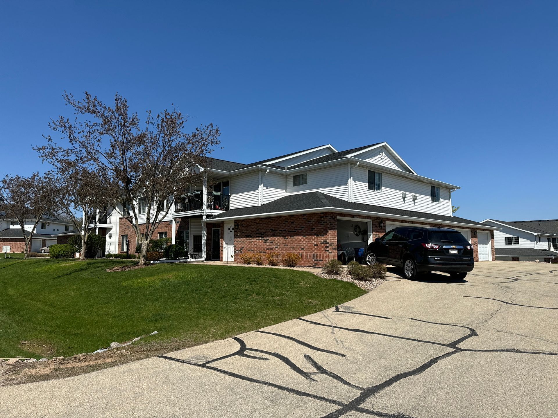 A two-story white house with brick accents and a black SUV parked in the driveway on a sunny day.