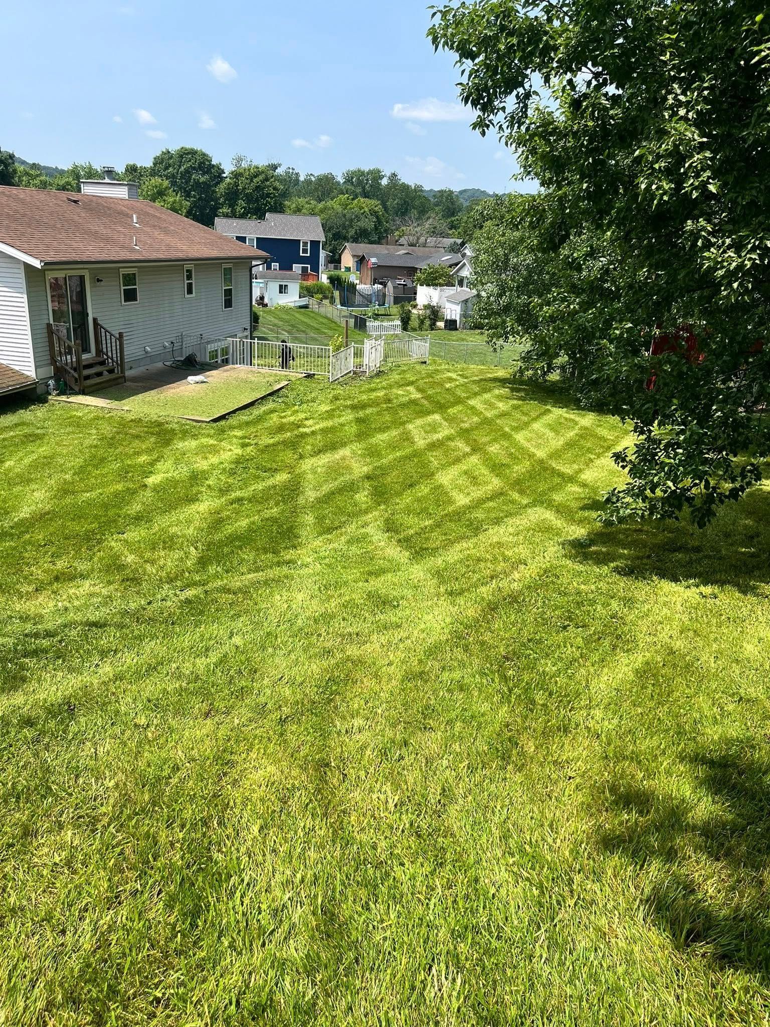 A lush green lawn with a crisscross mowing pattern, adjacent to a residential house under a bright blue sky.