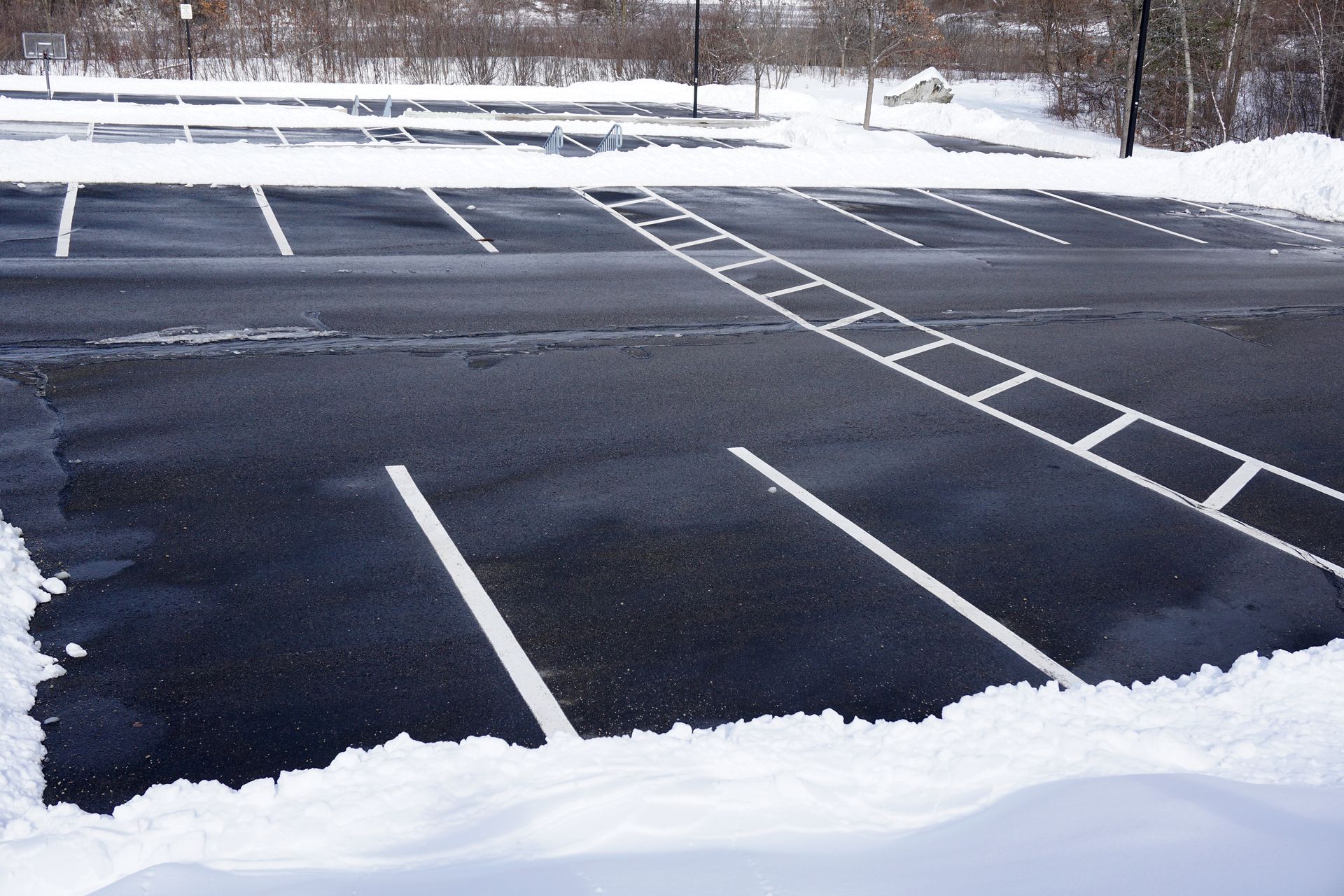 An asphalt parking lot with white painted markings, partially covered in patches of snow. An asphalt parking lot with white painted markings, partially covered in patches of snow.