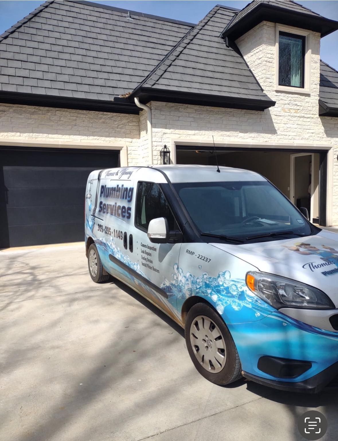 Plumbing services van parked in a driveway in front of a house with the garage door open.