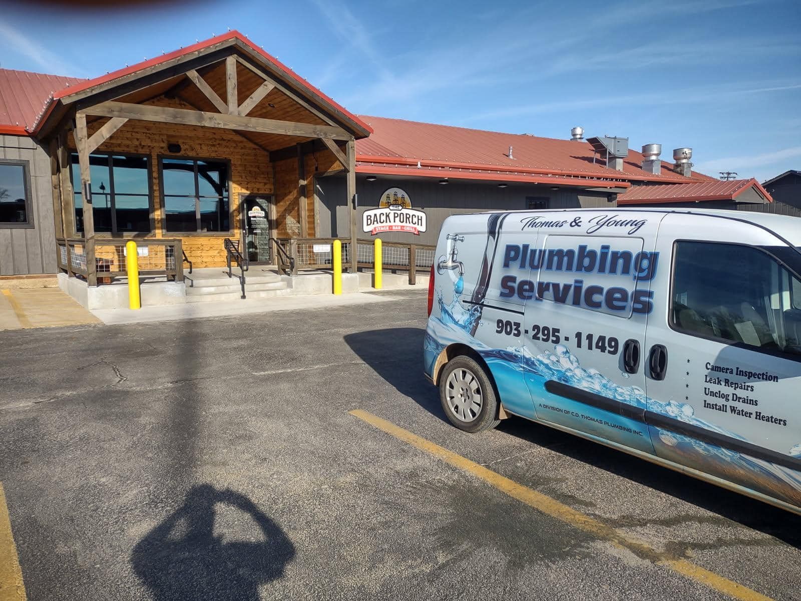 Plumbing service van parked in front of a restaurant with a rustic wooden facade on a sunny day.