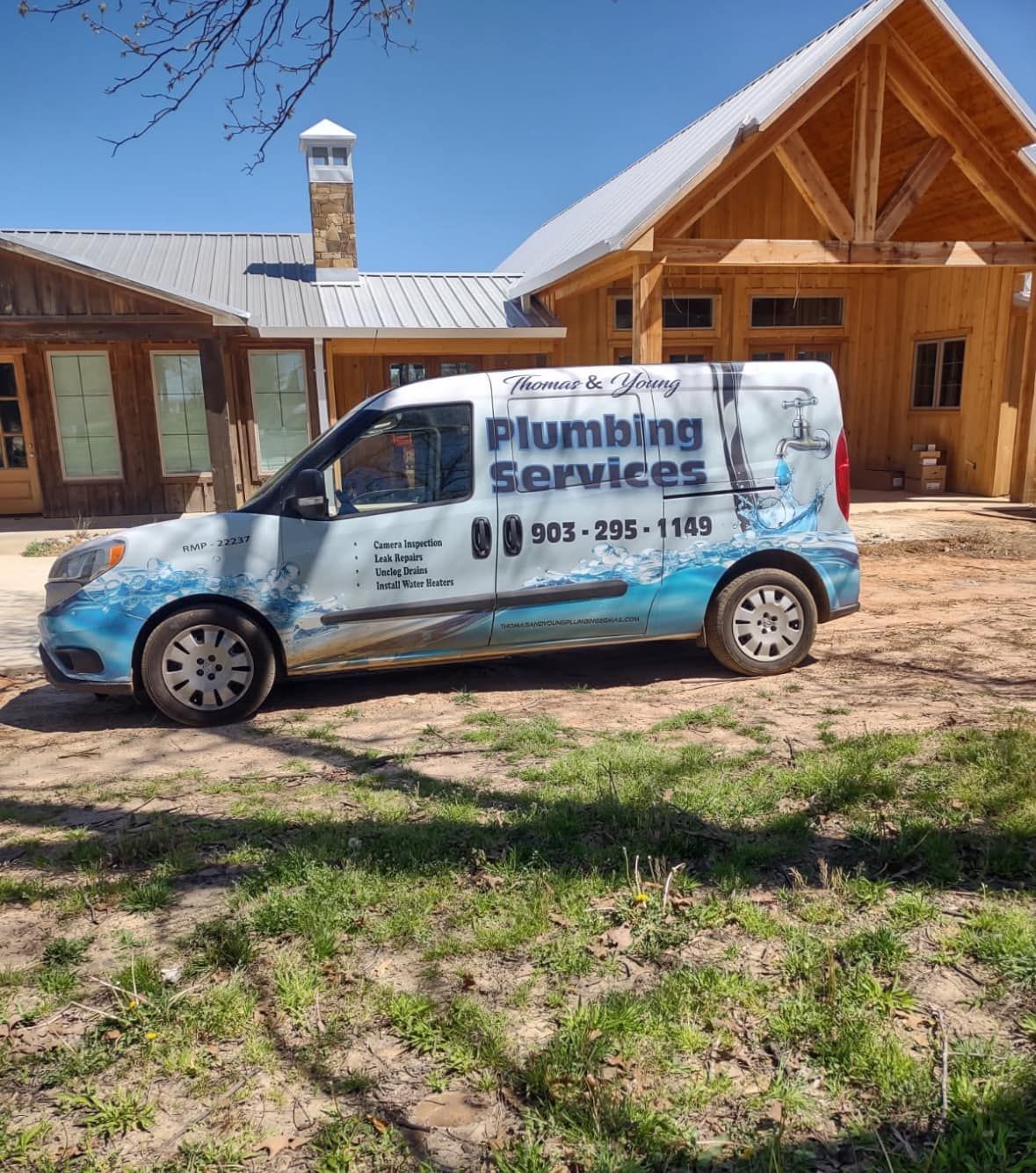 Plumbing services van parked on grass near a wooden building, phone number 933-205-1979 visible.