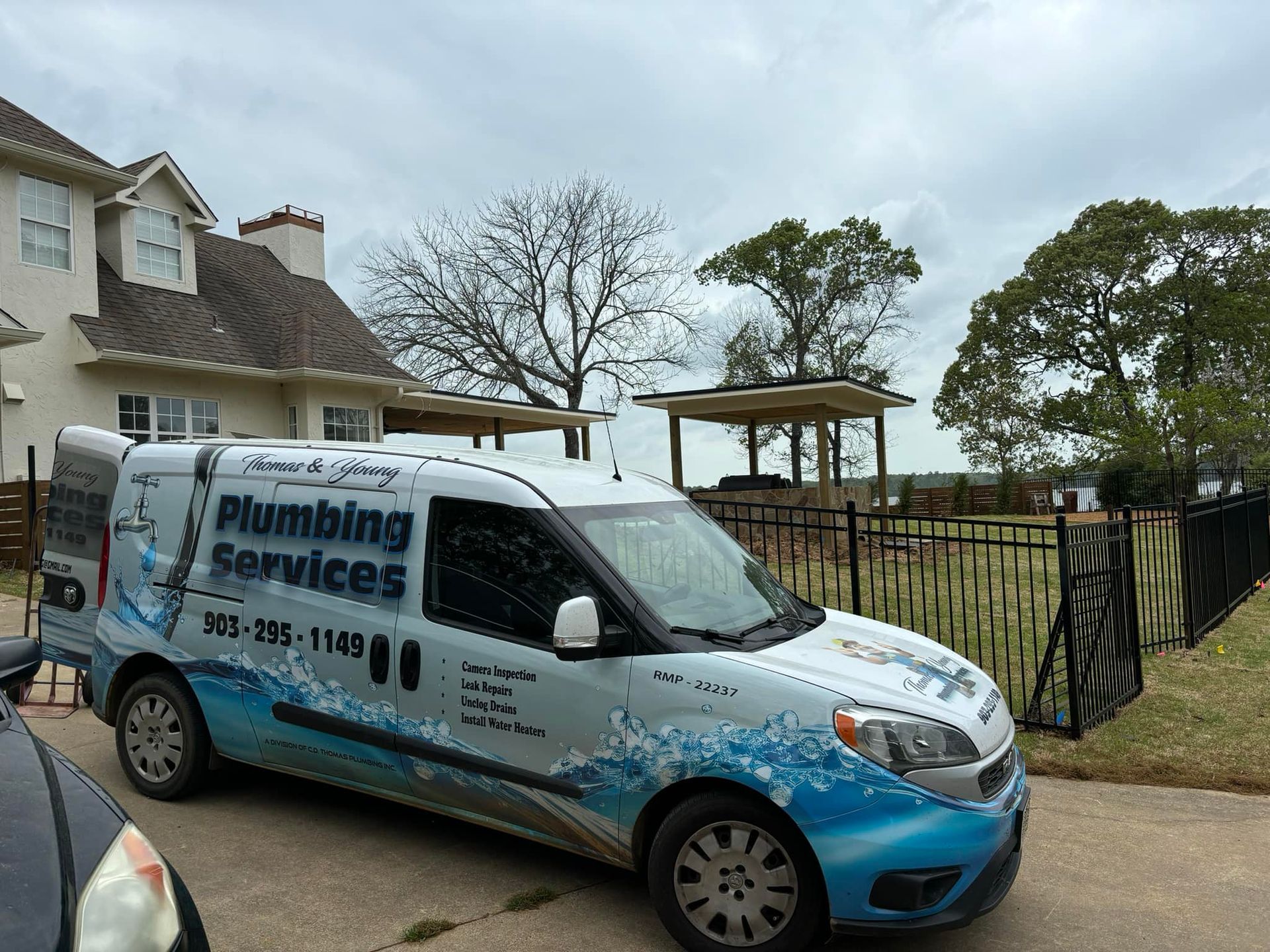Plumbing service van parked in front of a house. The van has the business name and phone number on it.