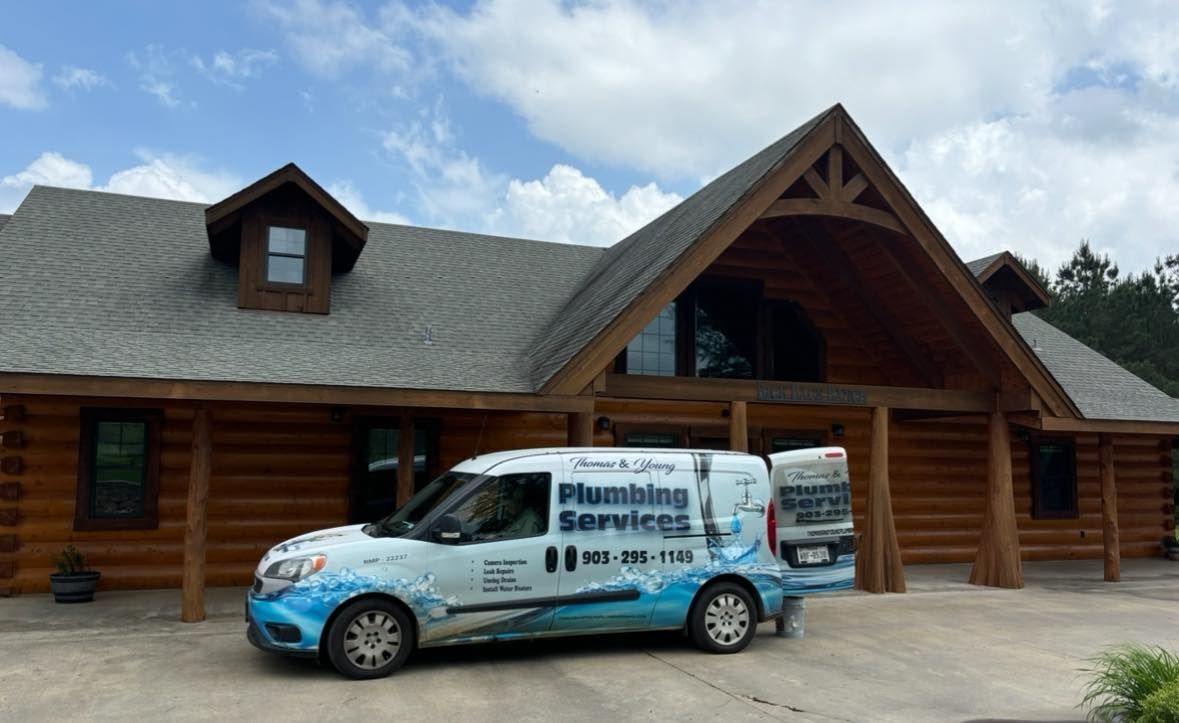 White plumbing service van parked in front of a log cabin style building.