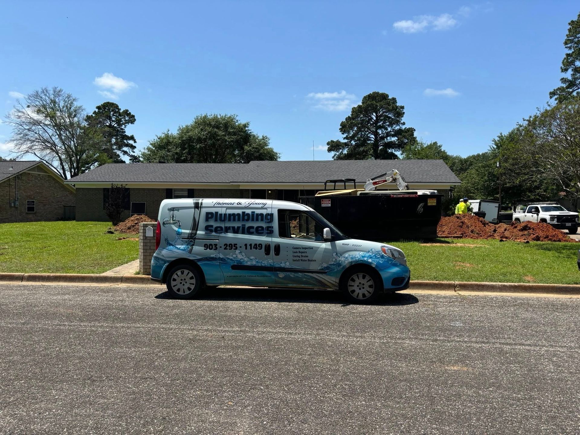 Plumbing van parked in front of a house under construction; blue sky, sunny day.