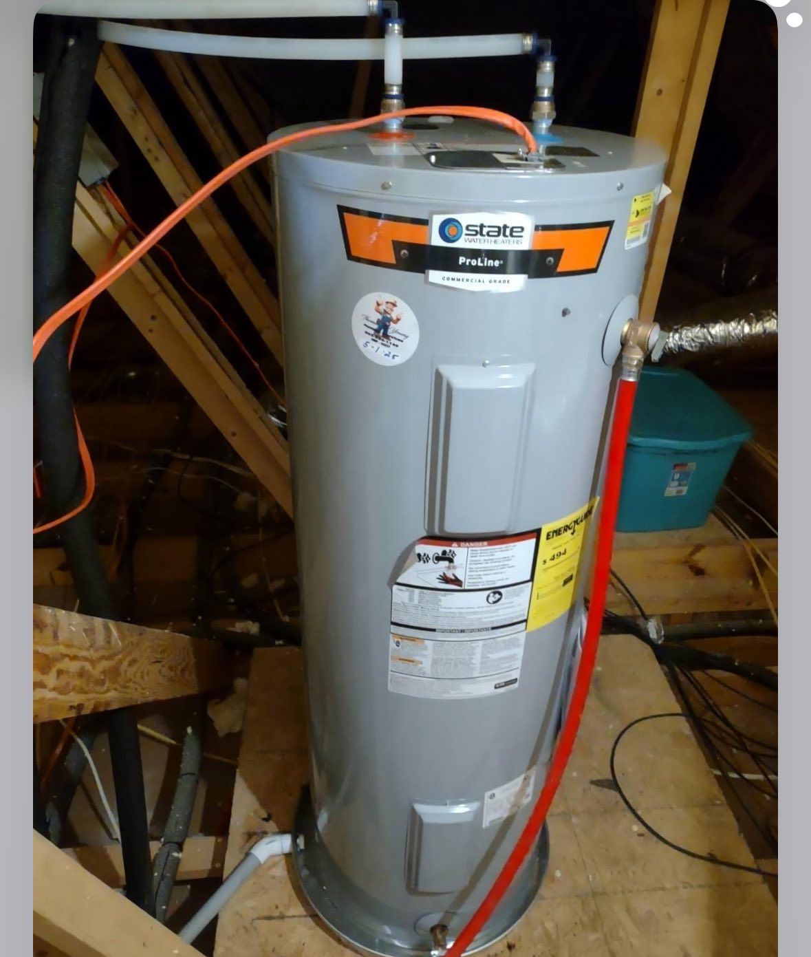 A tall, gray water heater with pipes in an attic setting.