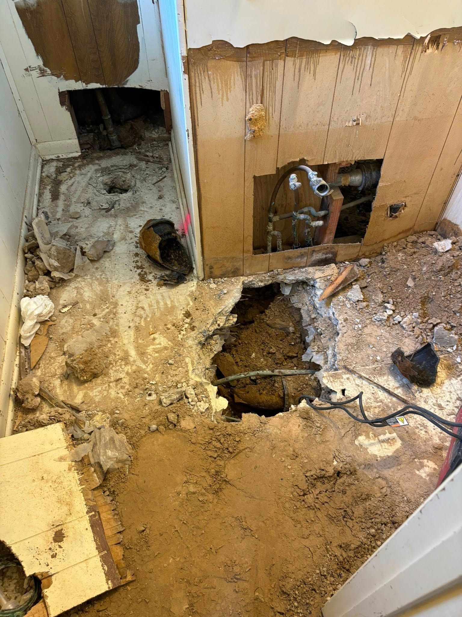 Room gutted; holes in floor and walls, debris scattered. Plumbing visible.