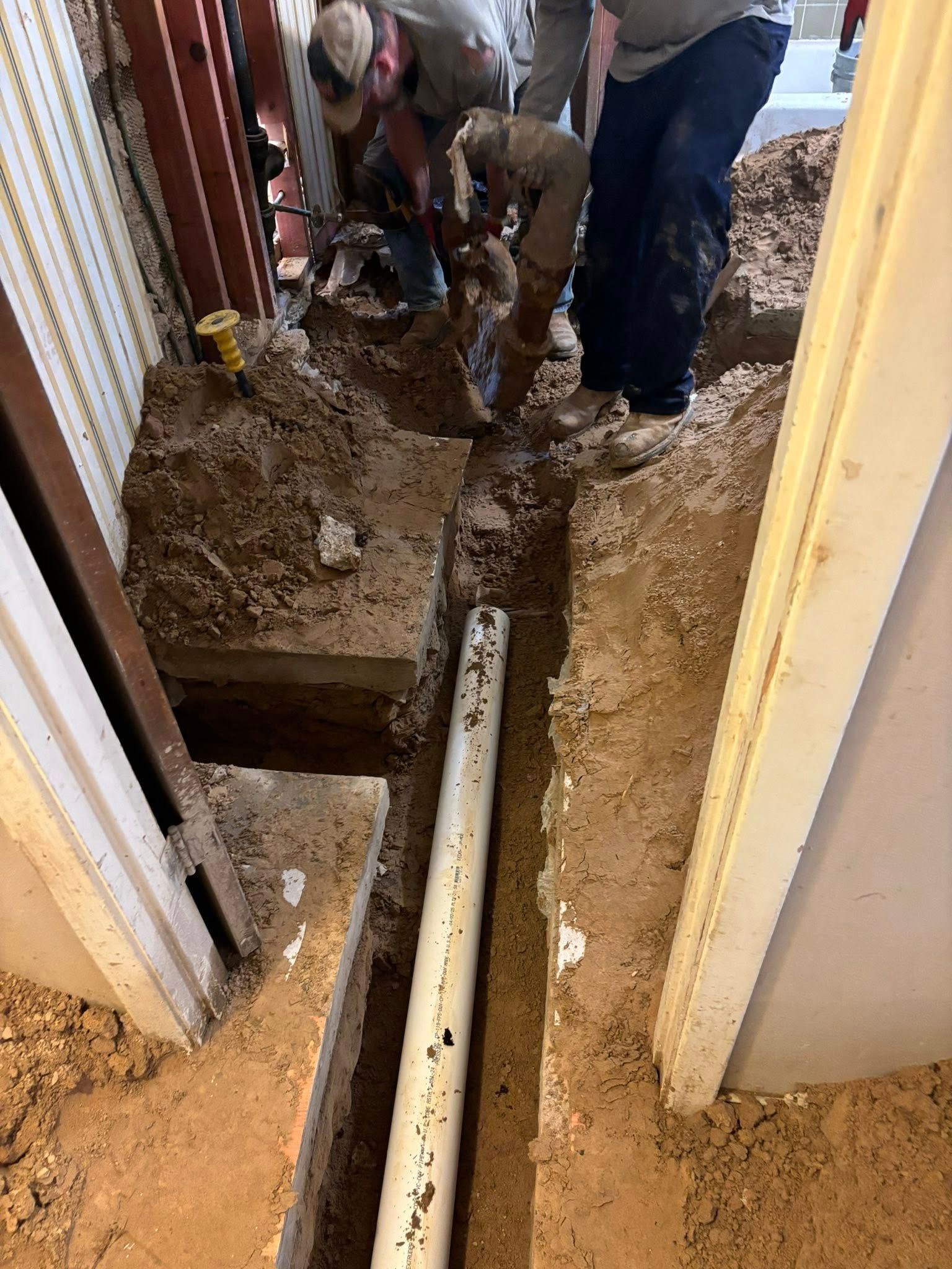 Workers digging a trench around a white pipe. The workers are in an indoor setting.