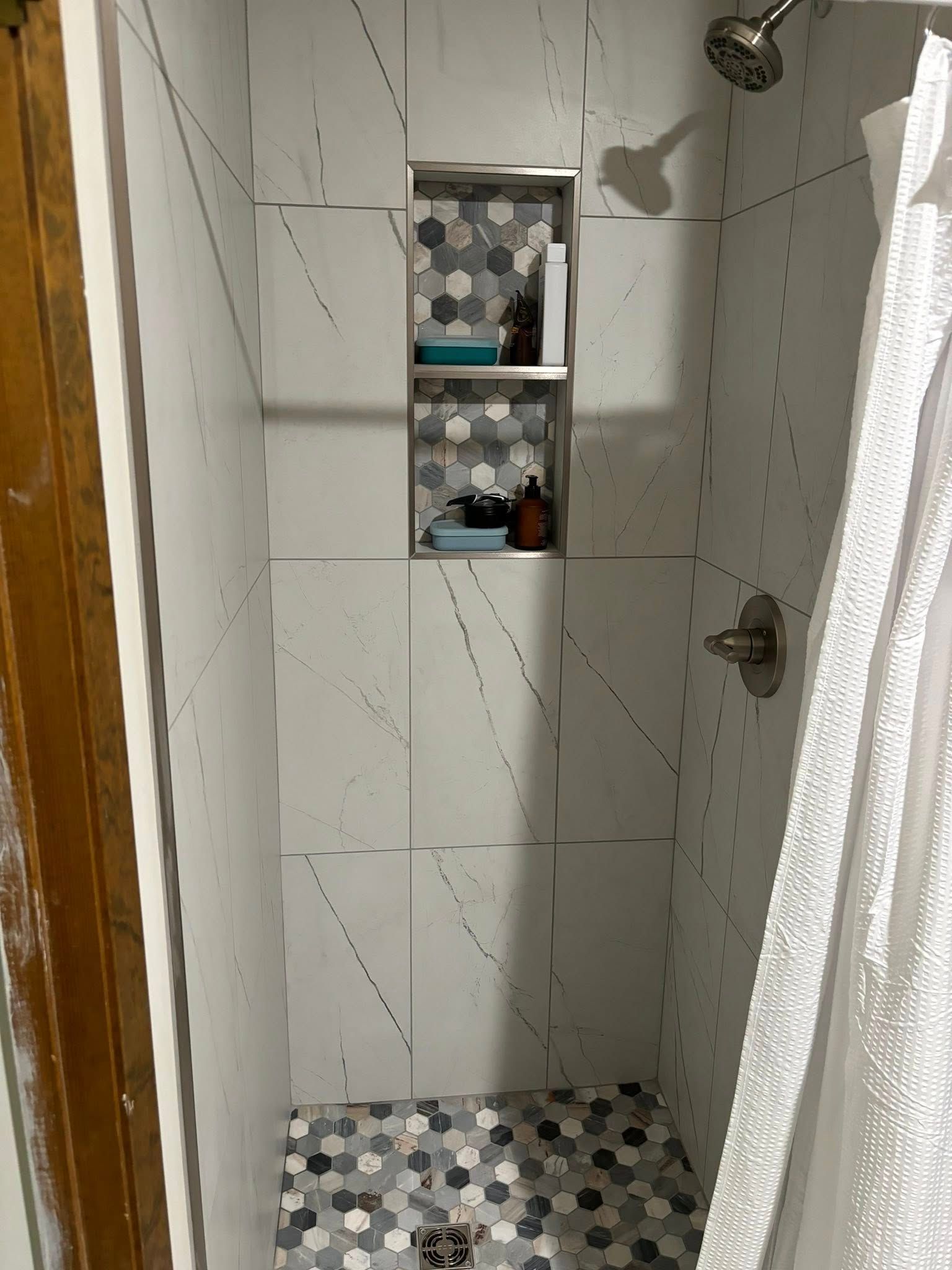 Tiled shower with a built-in shelf. White and gray hexagonal tiles on the floor. White walls with gray accents.