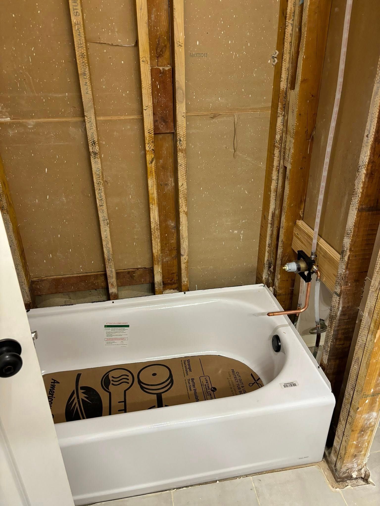 A white bathtub sits between exposed wall studs in a bathroom under construction.