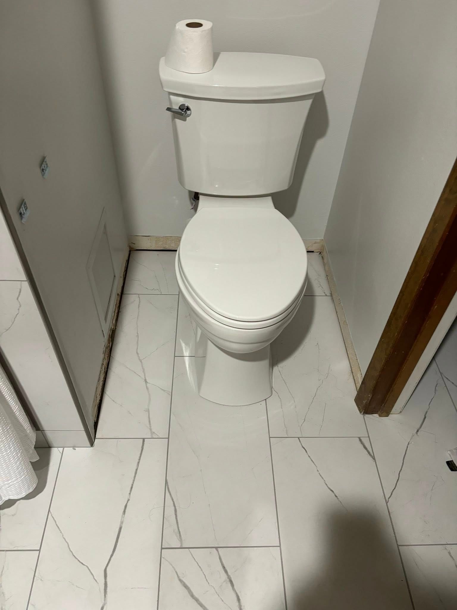 Toilet in a small bathroom with white tiles and a roll of toilet paper on the tank.