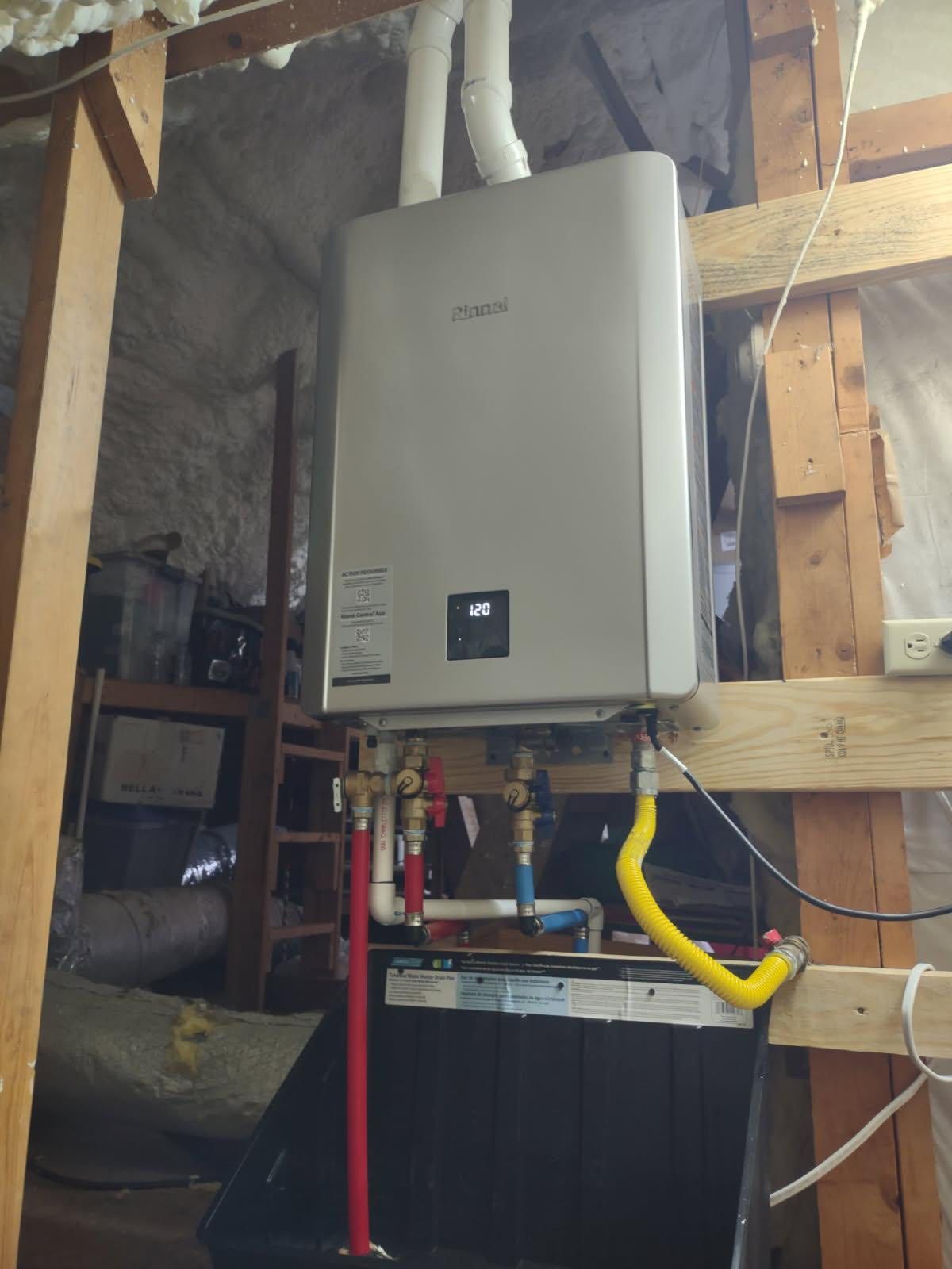Tankless water heater installed in an unfinished space. It has white piping and gas lines.