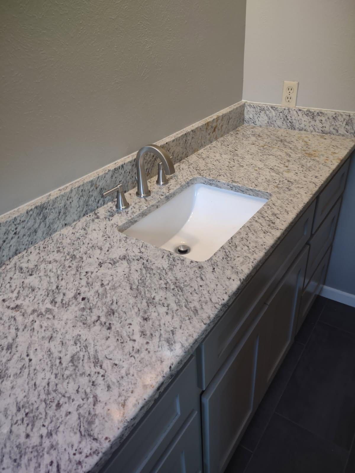 Bathroom vanity with white granite countertop, white sink, silver faucet, gray cabinets, and wall.