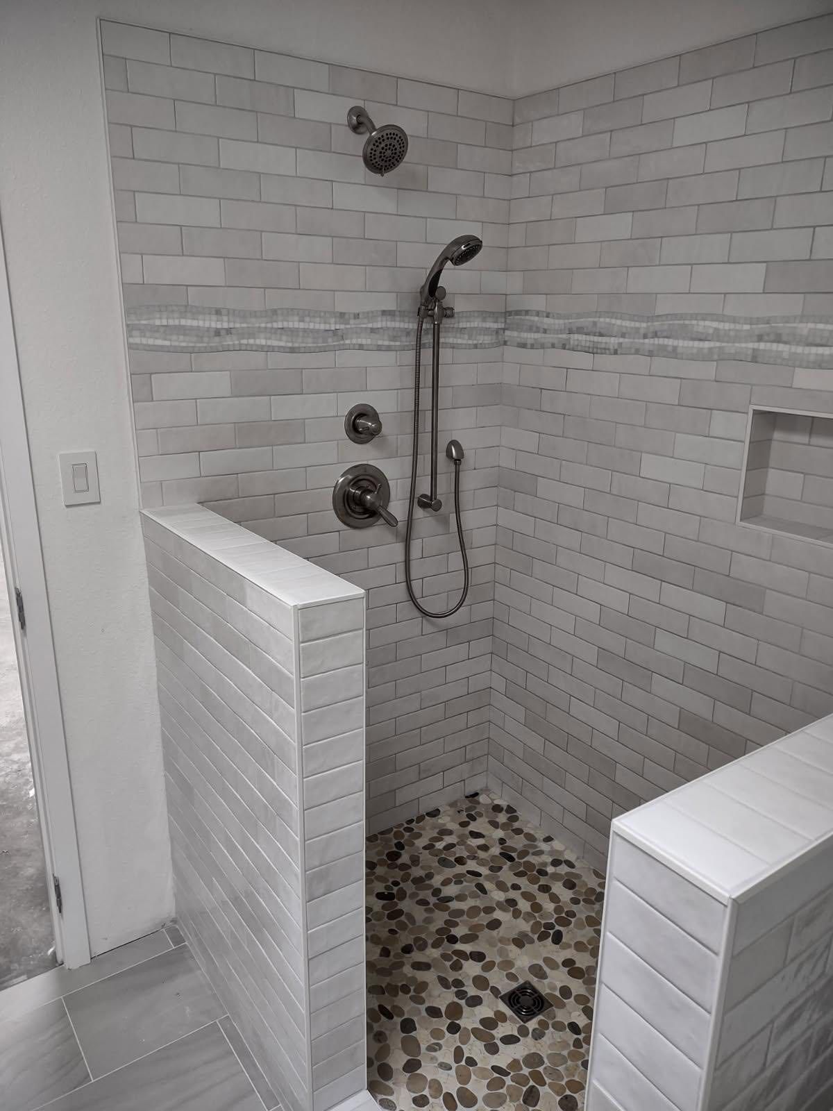 Tiled shower with pebble floor, gray brick-like walls, and two low walls with white edges.
