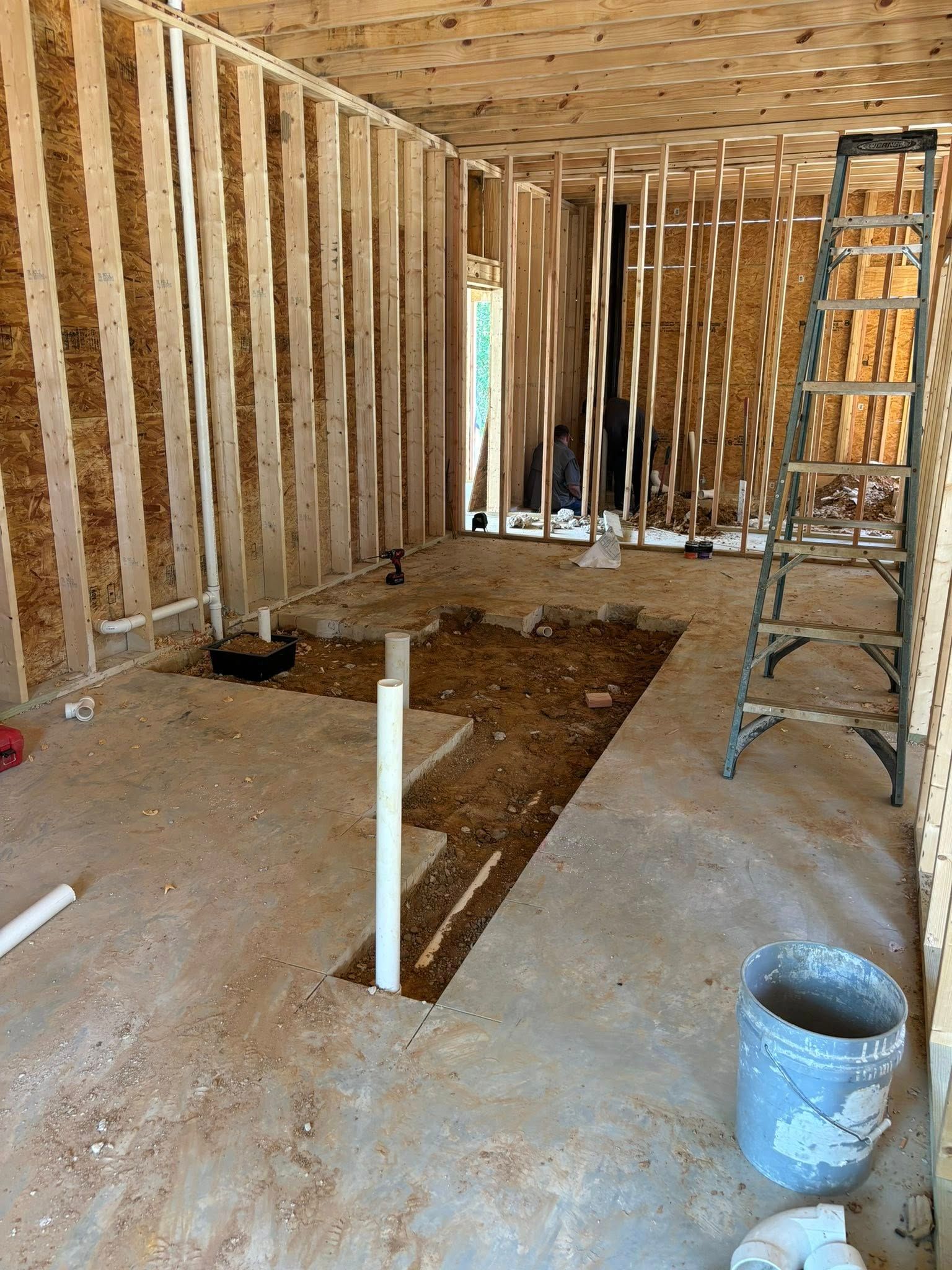 Interior construction: framed walls, plumbing in concrete floor, ladder, bucket.