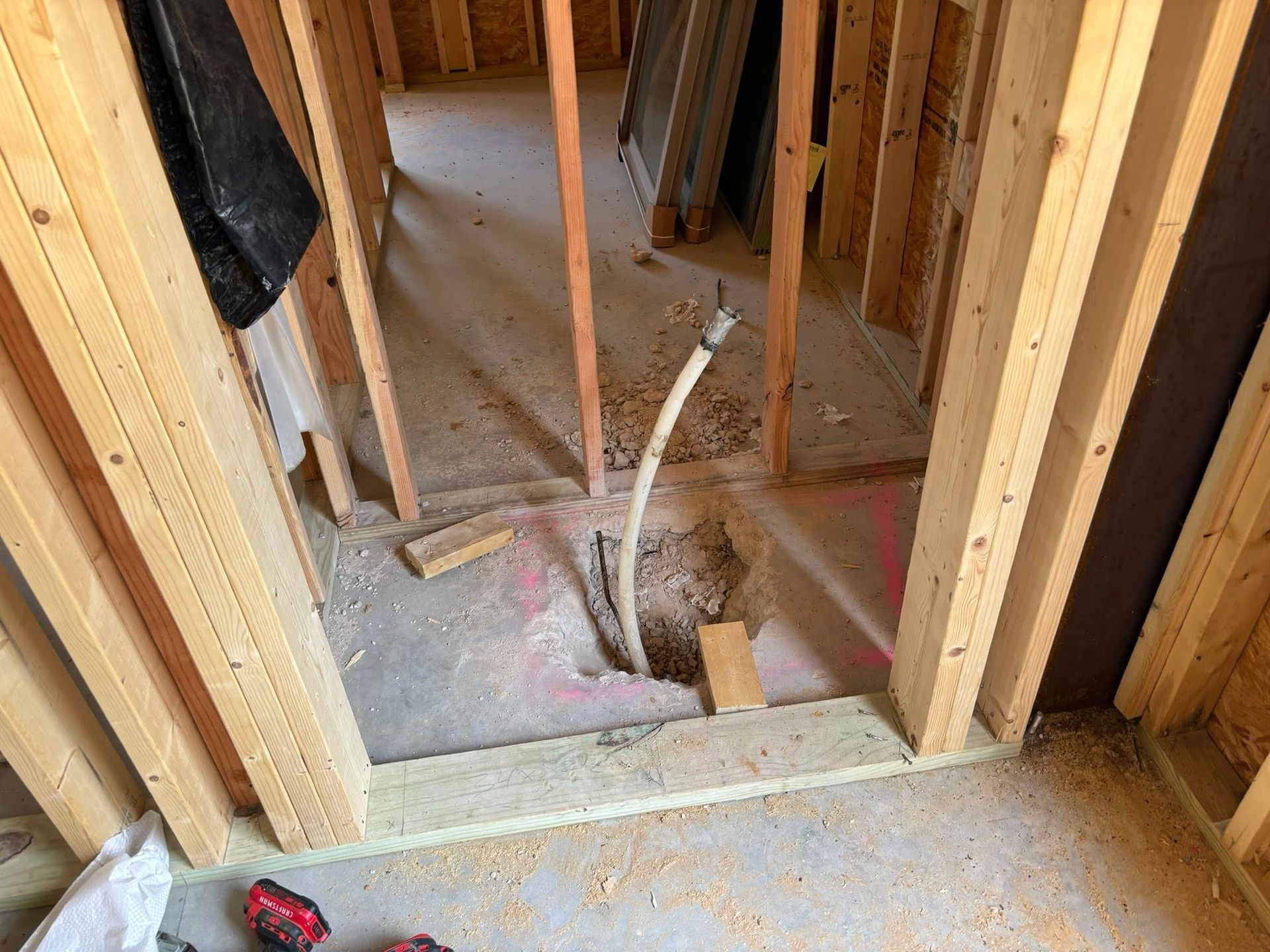 Interior construction framing with a hole in the floor and a white pipe extending up.