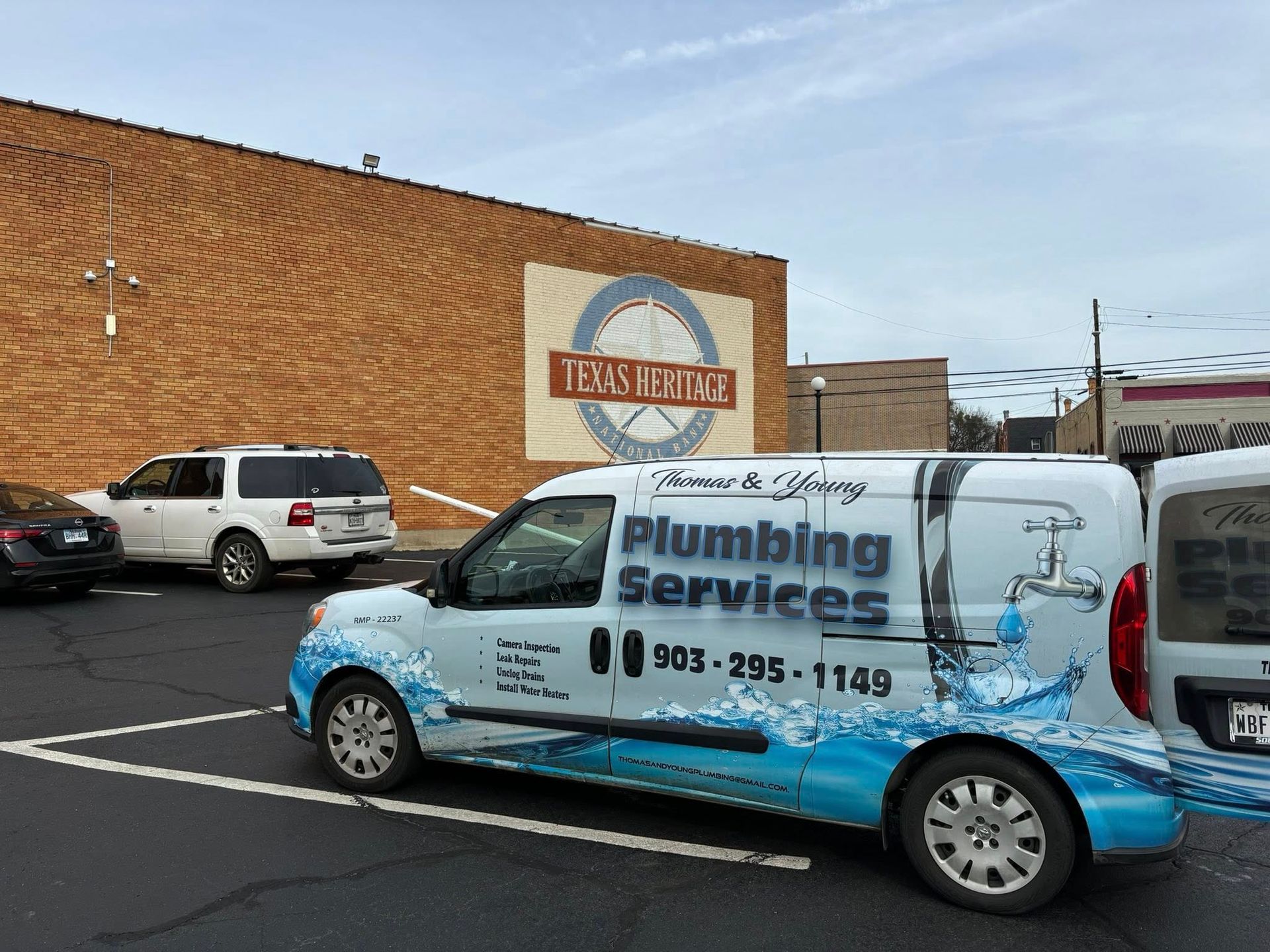Plumbing services van parked in front of brick building with sign 