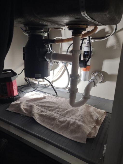 Underside of a kitchen sink with a garbage disposal and plumbing pipes. A towel lies below to catch drips.